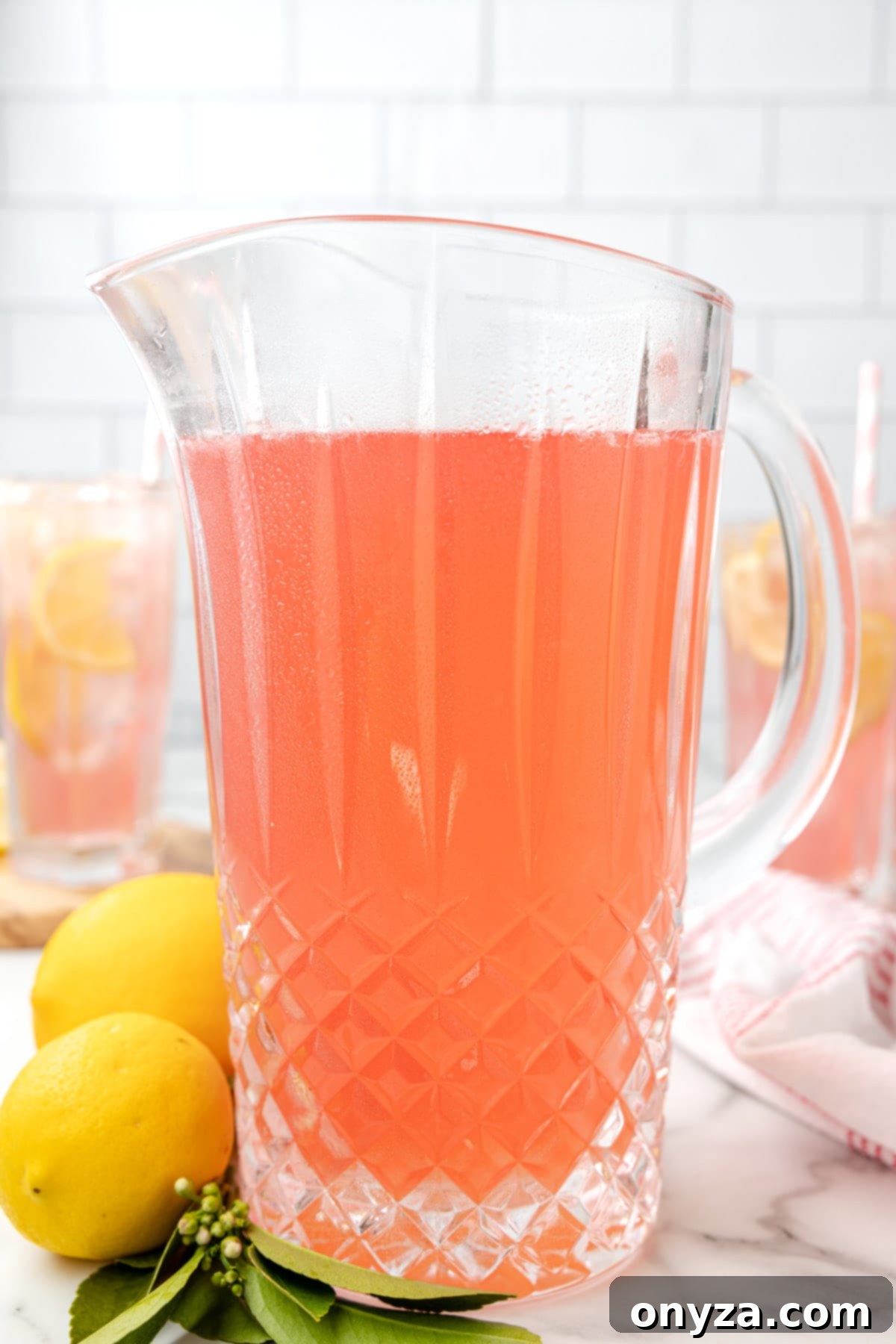 A large glass pitcher filled with a beautiful, light pink lemonade, garnished with fresh lemon slices, ready to be served.