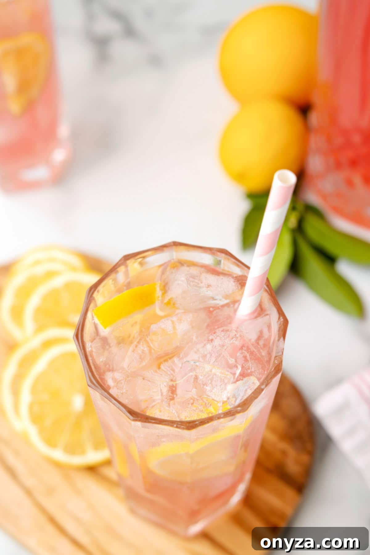 An overhead photo of a single glass of vibrant pink lemonade, garnished with a lemon slice, placed on a rustic wood serving board.