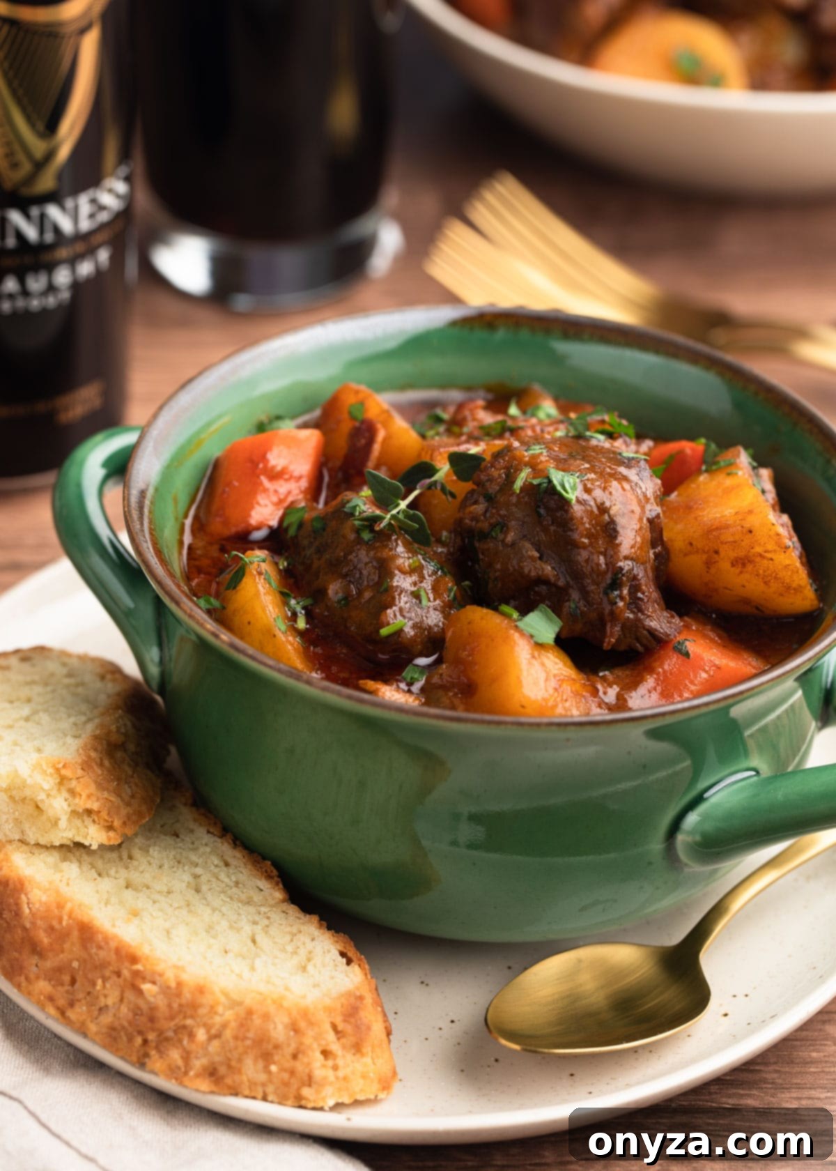 Slow-Cooked Guinness Beef Stew 2 Guinness Beef Stew in a green handled bowl on top of an ivory plate with slices of Irish Soda Bread and a gold tone spoon