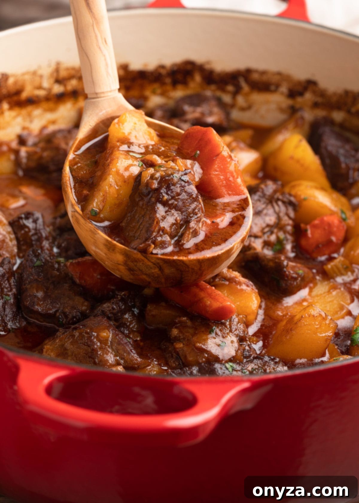 Slow-Cooked Guinness Beef Stew 7 ladleful of stout beef stew being scooped from a red Le Creuset Dutch oven