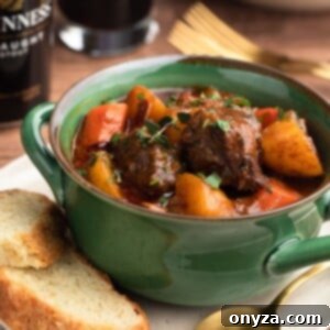 Slow-Cooked Guinness Beef Stew 9 Guinness Beef Stew in a green handled bowl on top of an ivory plate with slices of Irish Soda Bread and a gold tone spoon