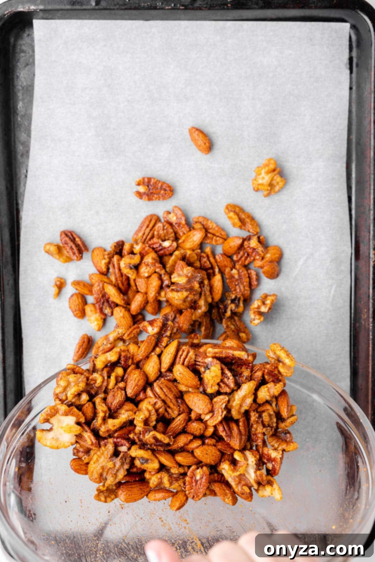 An overhead perspective showcasing a mixture of spicy nuts being carefully poured onto a baking sheet lined with parchment paper, preparing for baking.