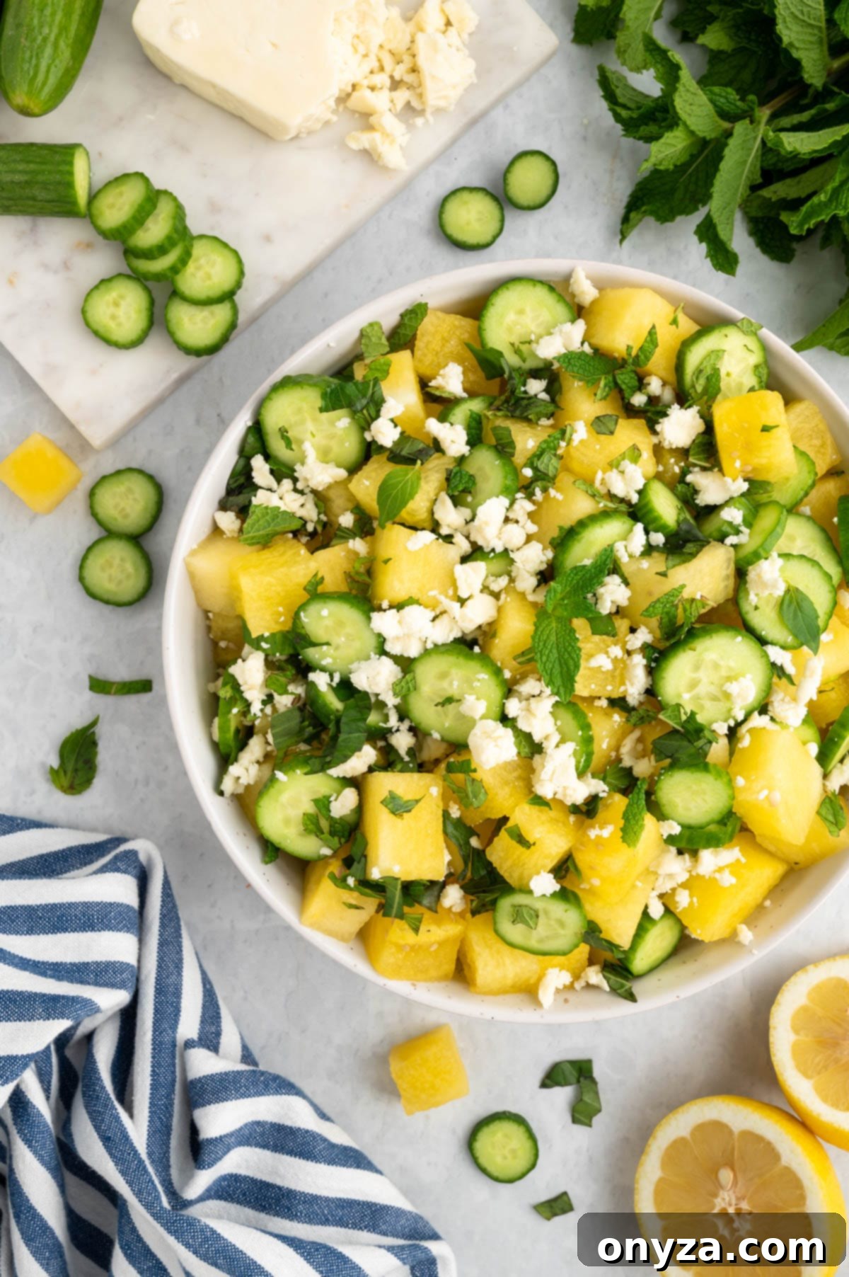 A dazzling Watermelon Feta and Cucumber Salad in a elegant white bowl, accompanied by a stylish blue and white striped napkin, ready to be served at a summer gathering.