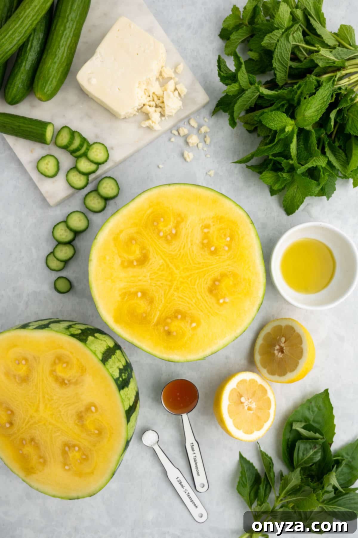 Overhead flat lay of essential ingredients for a refreshing Watermelon Feta Salad, featuring a halved yellow watermelon, bright lemon halves, freshly sliced Persian cucumbers, crumbled feta cheese, golden honey, premium olive oil, and an assortment of aromatic herbs on a minimalist gray background.
