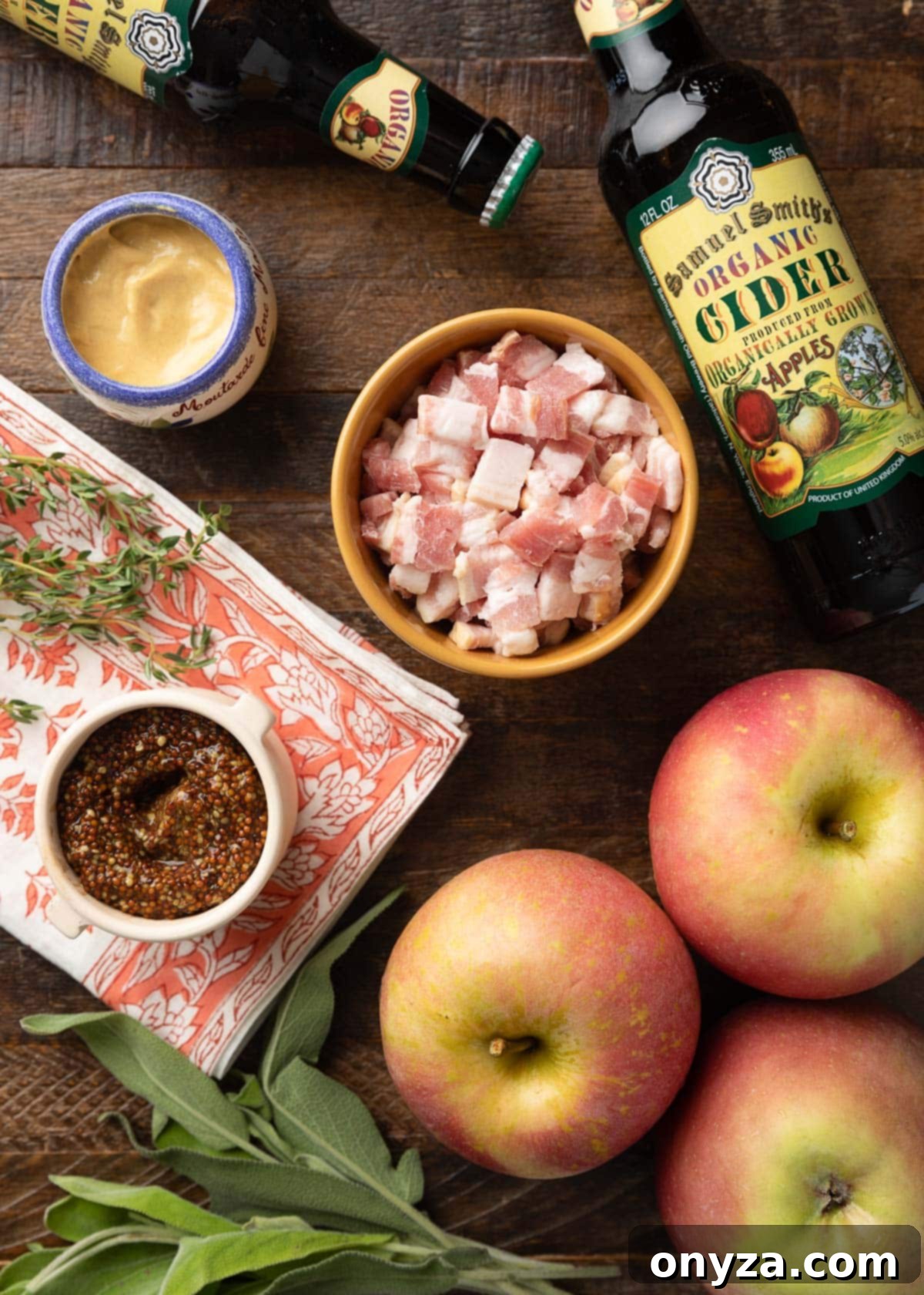 Cider-Braised Chicken with Crispy Bacon and Apples 3 Overhead view of various ingredients for Hard Cider Chicken: bottles of hard cider, pots of smooth and grainy Dijon mustard, freshly chopped bacon, crisp apples, and aromatic fresh herbs, arranged on a rustic wooden board.