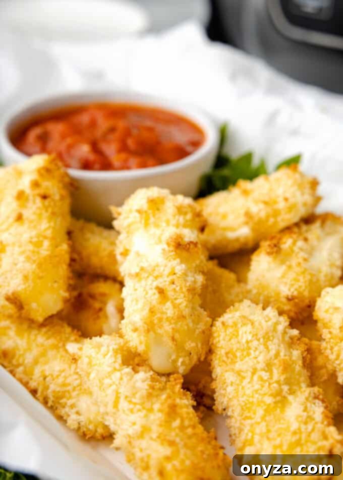 Crispy air fried mozzarella sticks on a parchment-lined platter with a bowl of vibrant marinara sauce, ready for dipping.