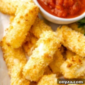 Overhead closeup of perfectly golden air fried mozzarella sticks on a platter with a bowl of marinara sauce, ready to be served.