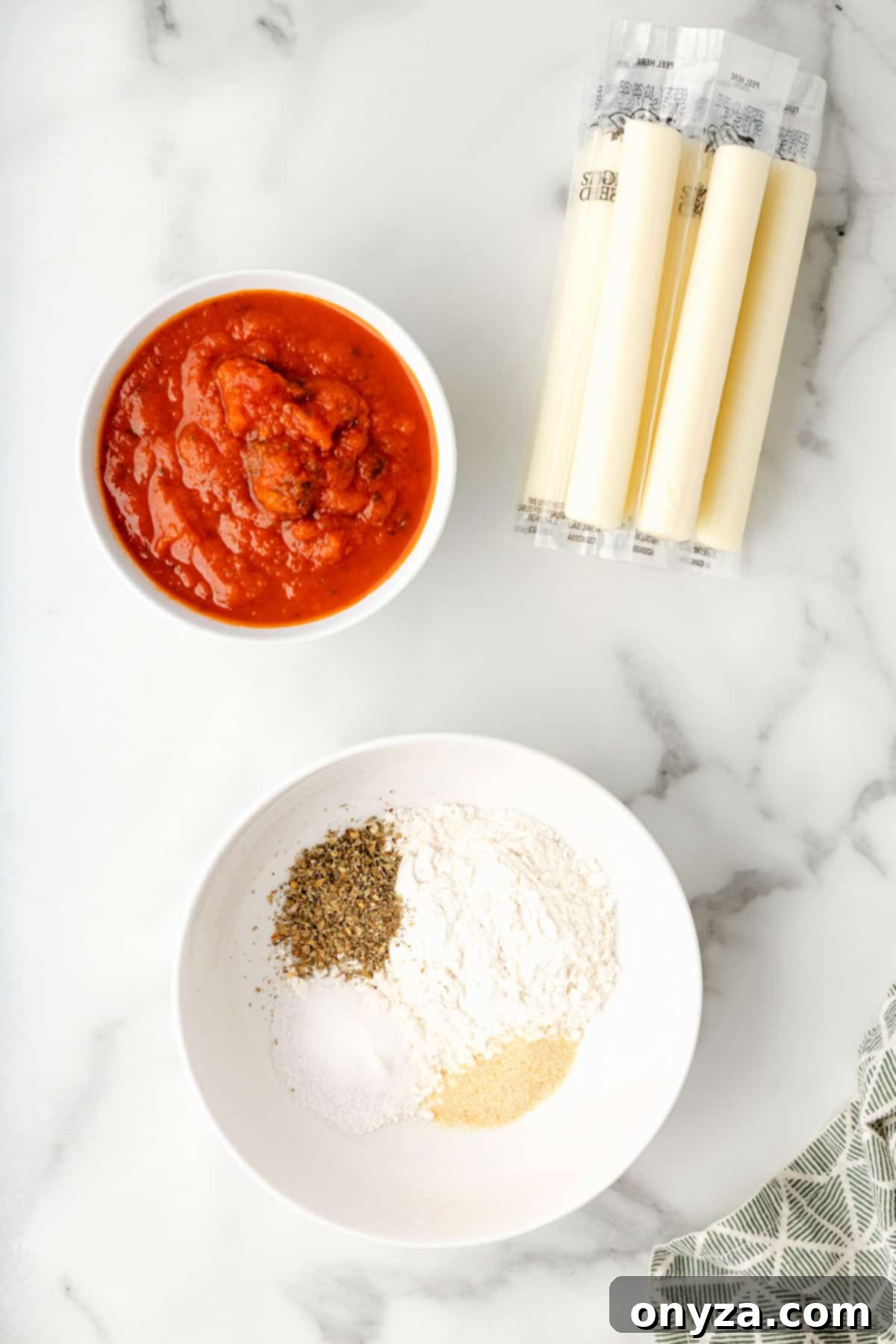 Overhead view displaying separate bowls of seasoned flour, marinara sauce, and wrapped string cheese on a white marble board, highlighting the key ingredients.