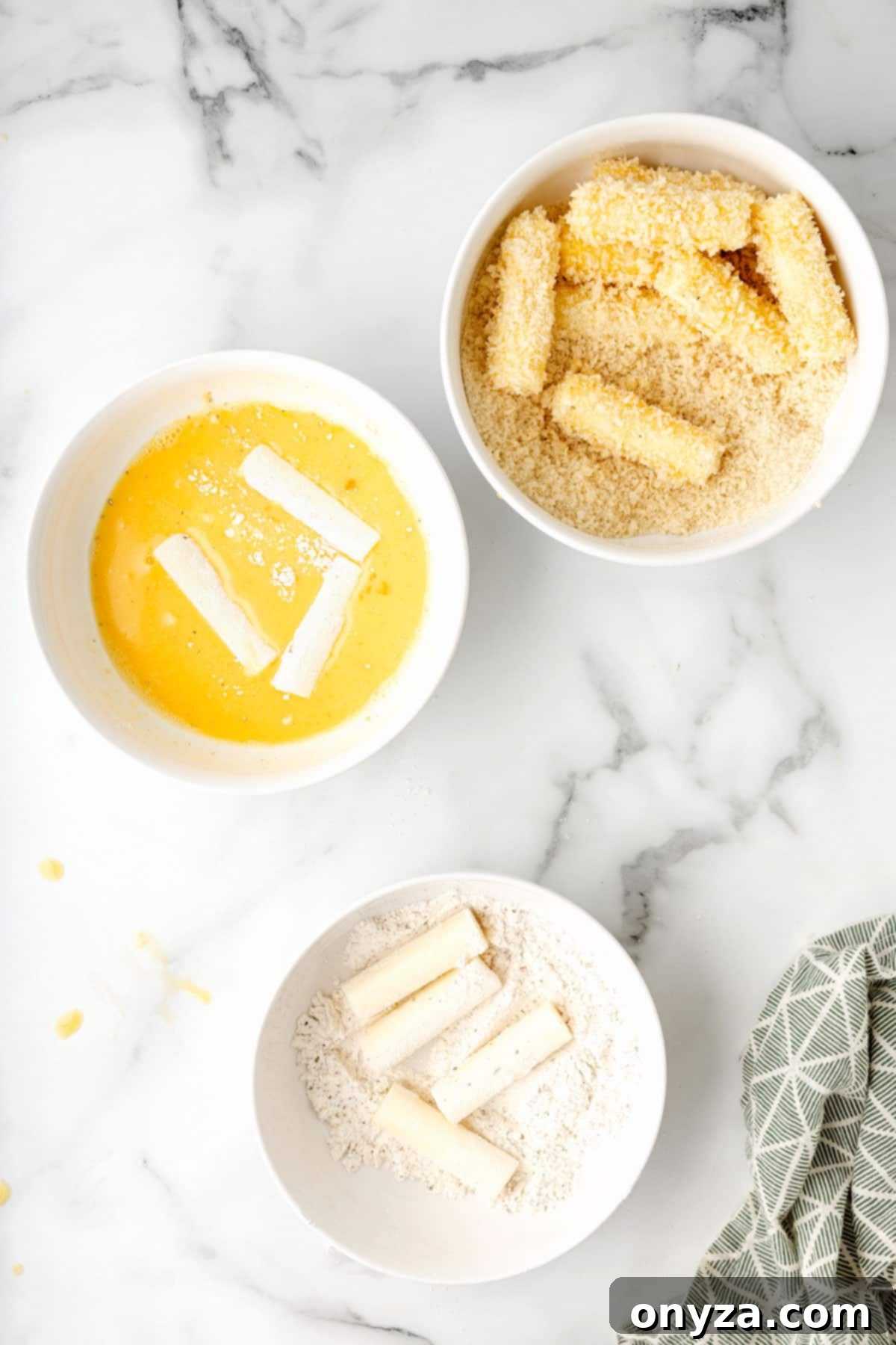 Overhead view of three bowls demonstrating the breading process for mozzarella sticks: seasoned flour, egg wash, and crispy Panko breadcrumbs.