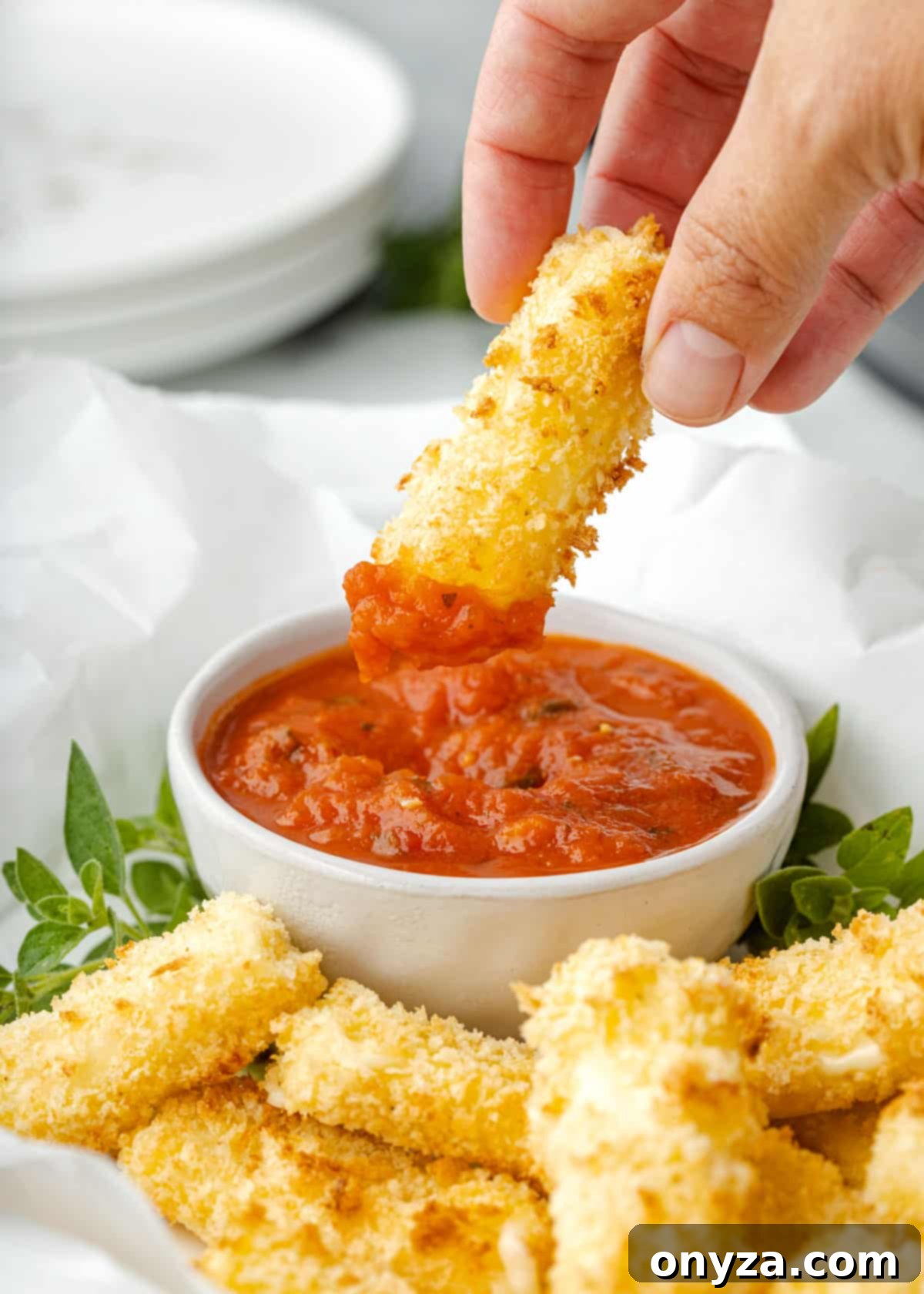 Close-up of a hand dipping a hot, air fried mozzarella stick into a bowl of rich red marinara sauce.