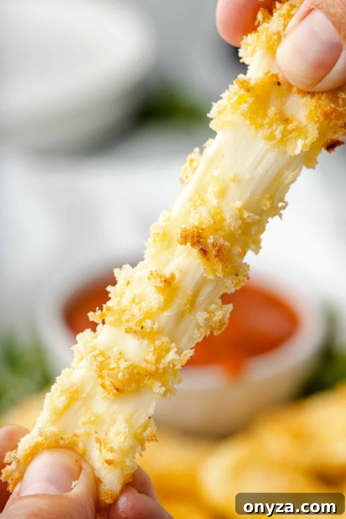 Close-up shot of a freshly air fried mozzarella stick being pulled apart, showcasing its irresistible, stringy melted cheese interior.