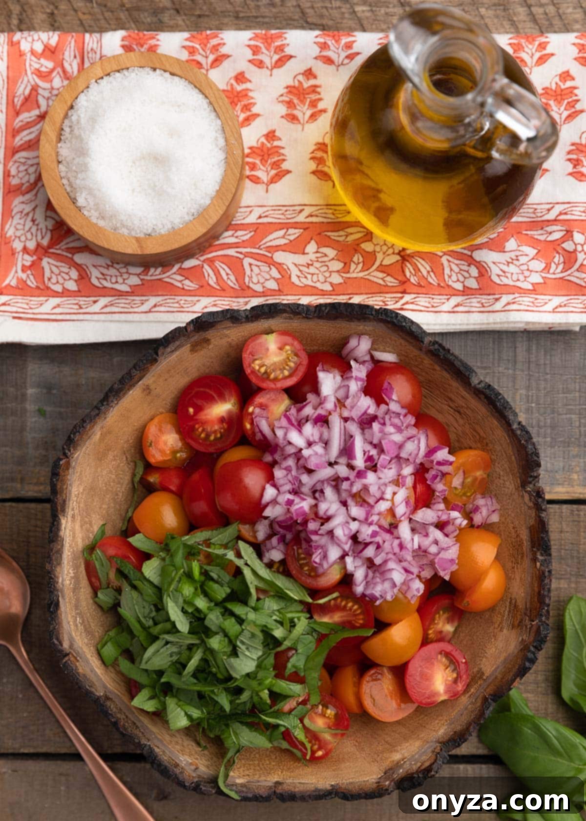 Fresh Cherry Tomato Bruschetta 4 overhead photo of halved cherry tomatoes, basil, and chopped red onion in a wooden bowl, beneath a bowl of sea salt and a cruet of olive oil