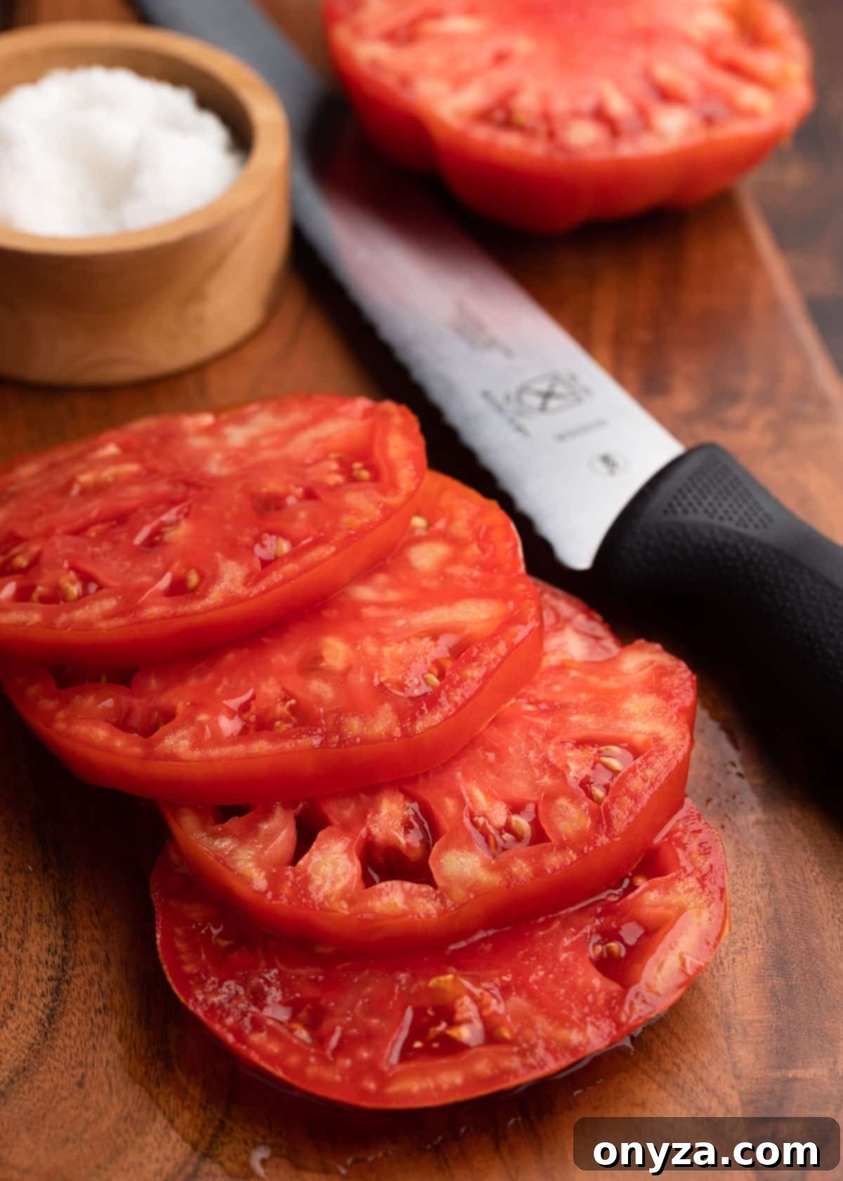 Sun-Kissed Southern Tomato Sandwich 3 Sliced Brandywine tomato on a wooden cutting board with a serrated knife and a small bowl of sea salt