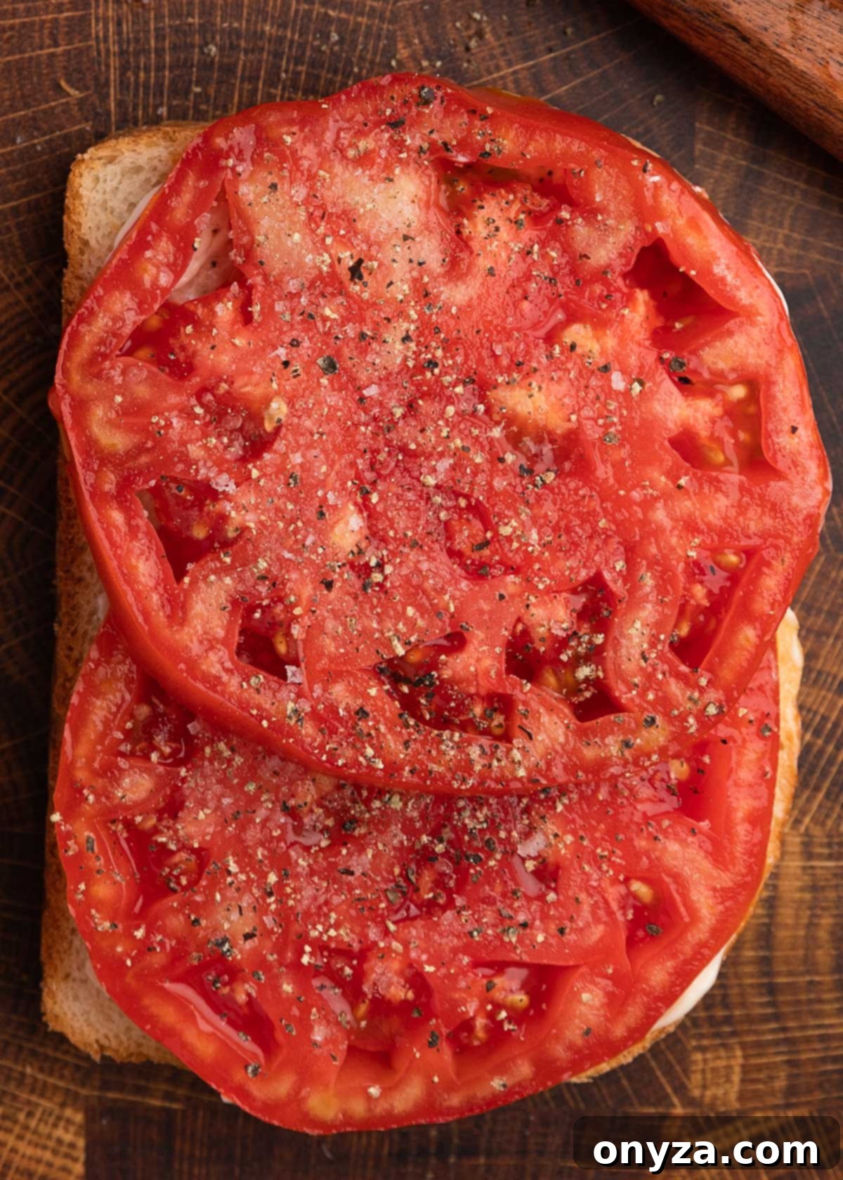 Sun-Kissed Southern Tomato Sandwich 7 Overhead close-up of thick tomato slices seasoned with salt and pepper, layered onto a slice of white bread generously spread with mayonnaise