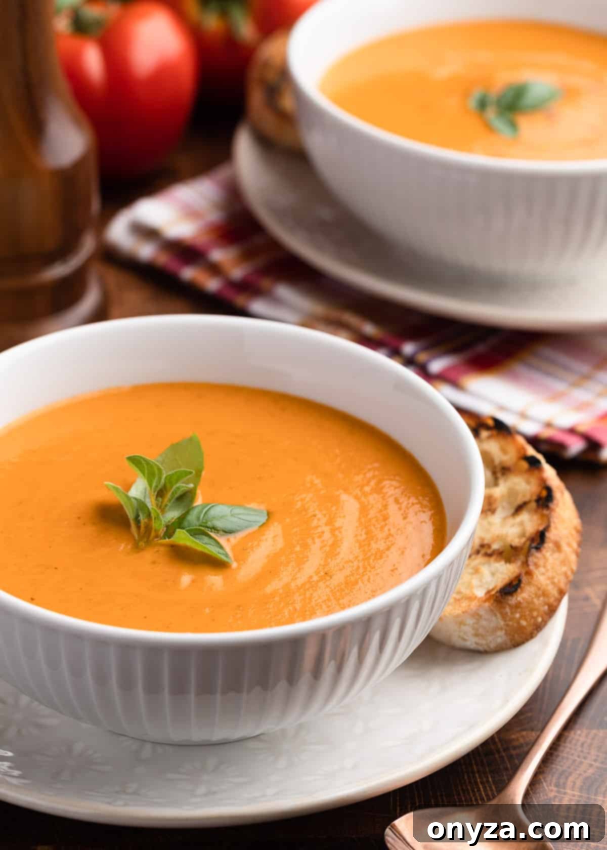 two white porcelain bowls of creamy roasted tomato soup with fresh basil garnish