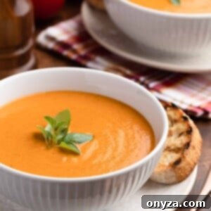 two white porcelain bowls of creamy roasted tomato soup with fresh basil garnish