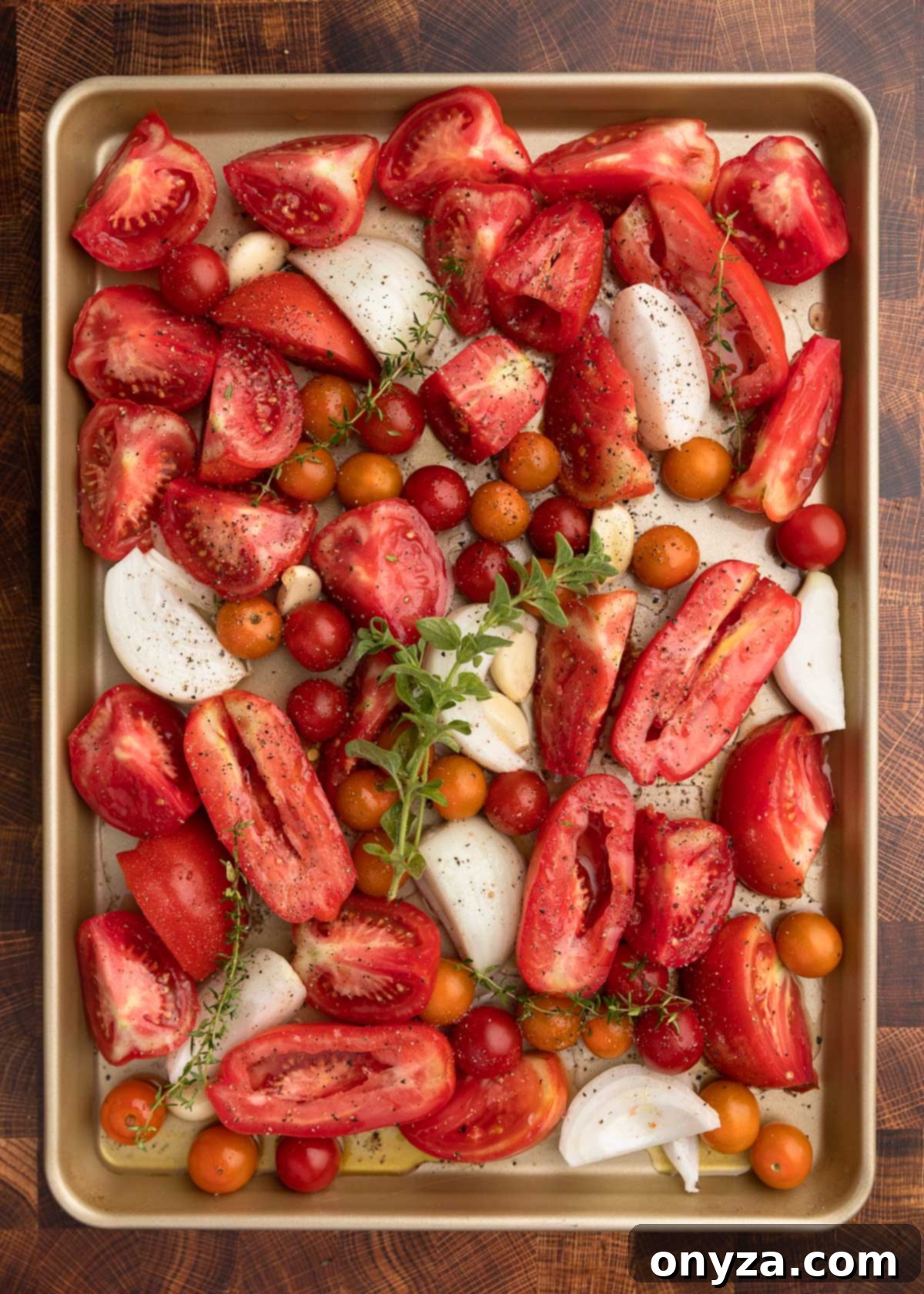 overhead photo of tomatoes, onions, garlic, and herbs on a baking sheet