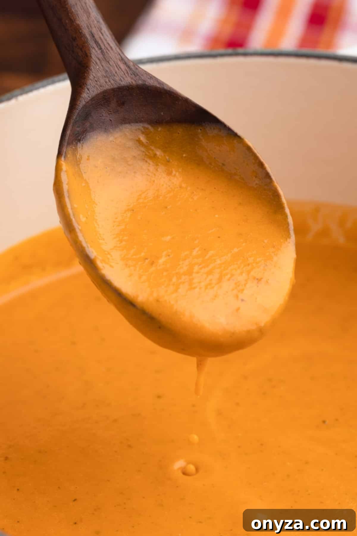 spoonful of creamy roasted tomato soup dripping into a white enameled cast iron pot