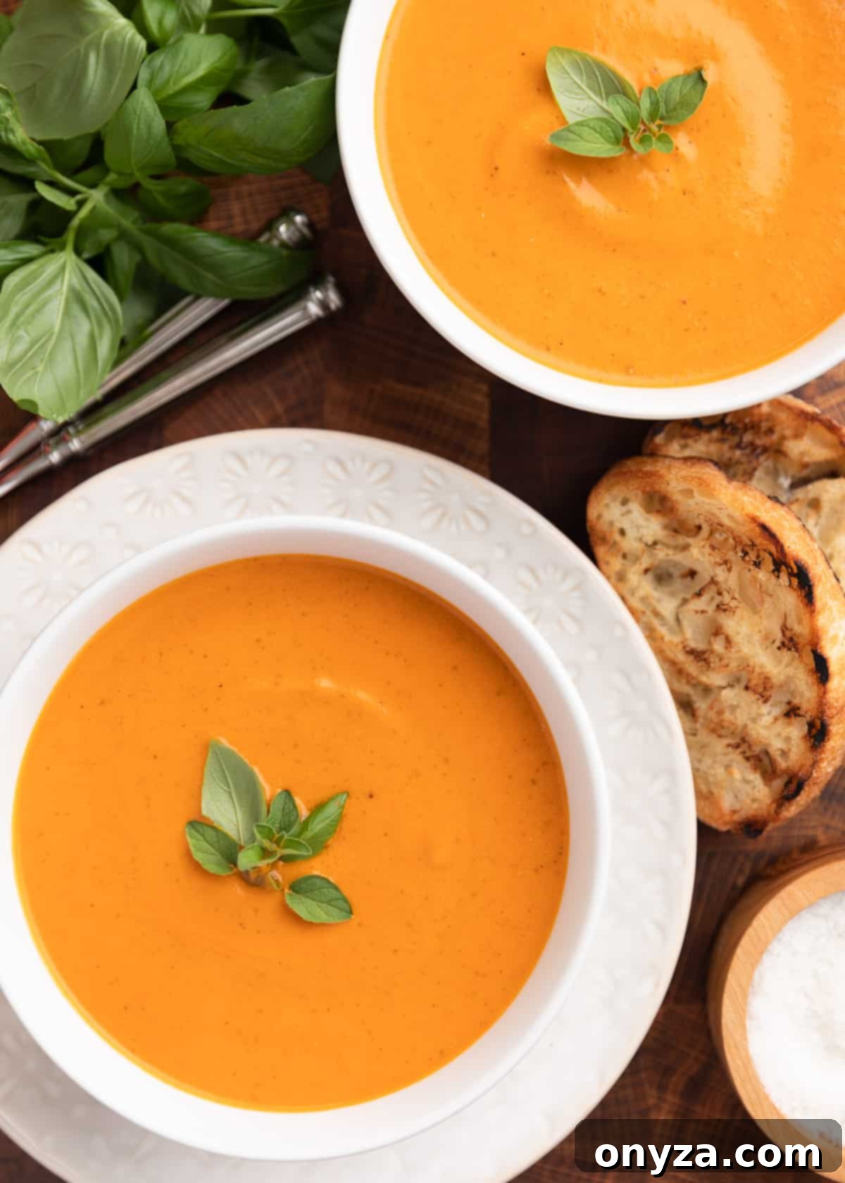 overhead photo of two bowls of creamy roasted tomato soup on a wood board