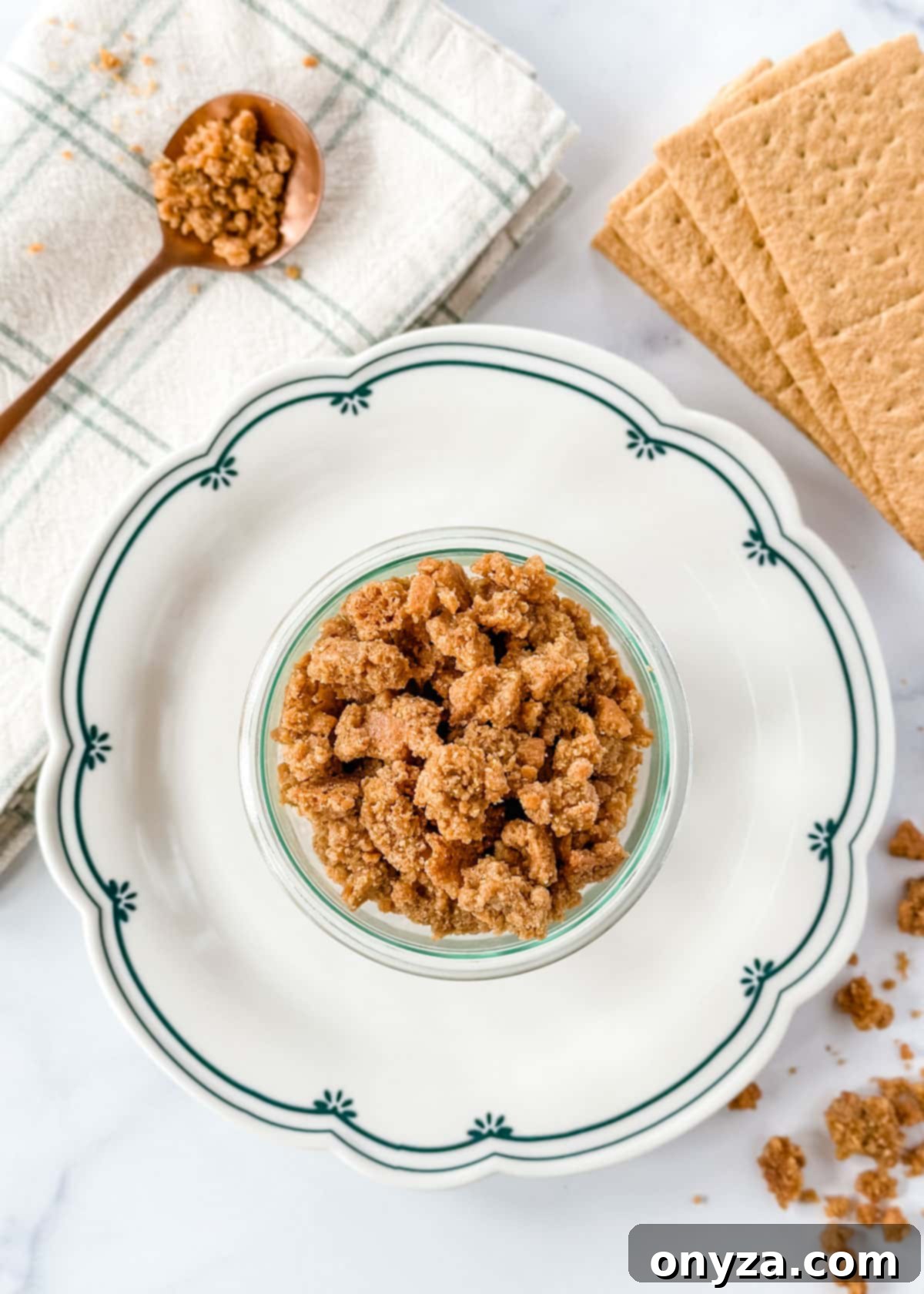 Overhead photo of a glass jar filled with golden graham cracker crumbles, resting on a decorative blue and white scalloped plate, highlighting its delicious texture.
