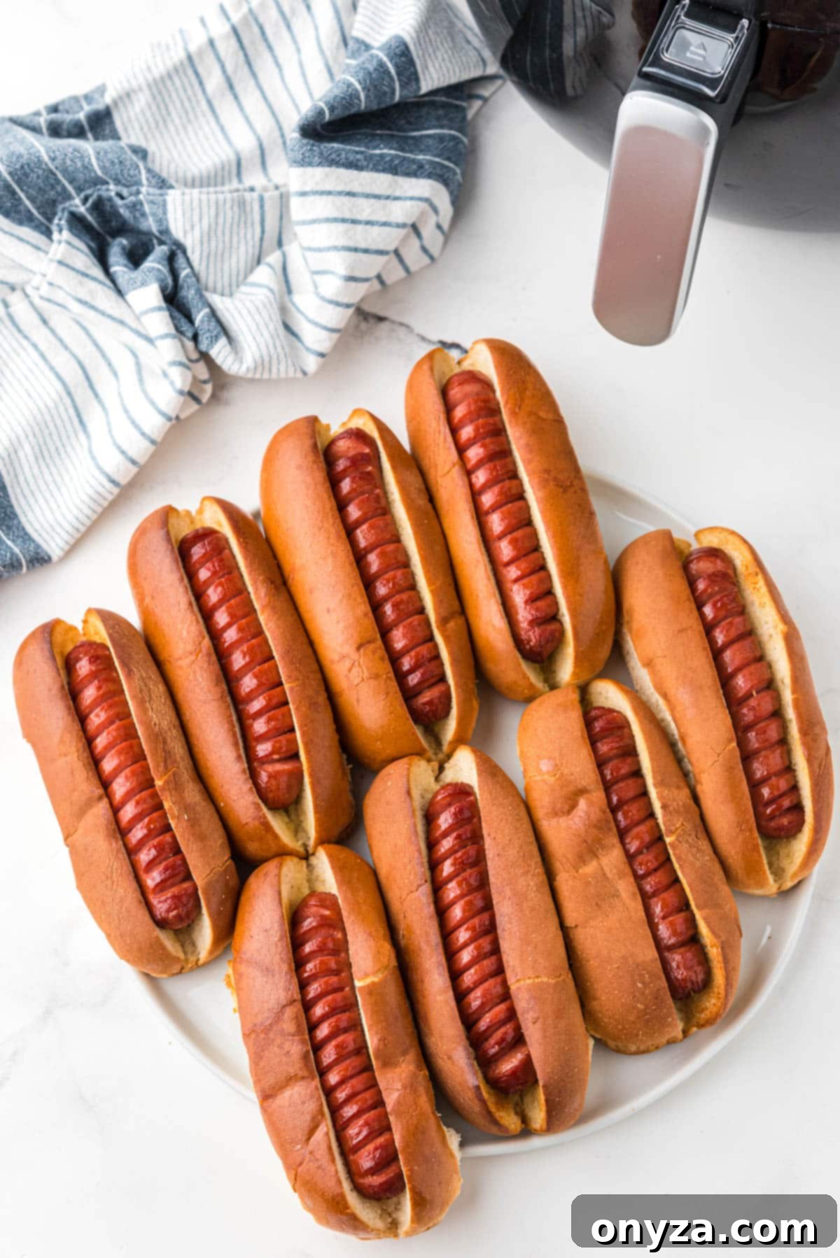An overhead shot showcasing eight delicious air fried hot dogs, nestled in their toasted buns, presented elegantly on a pristine white platter.