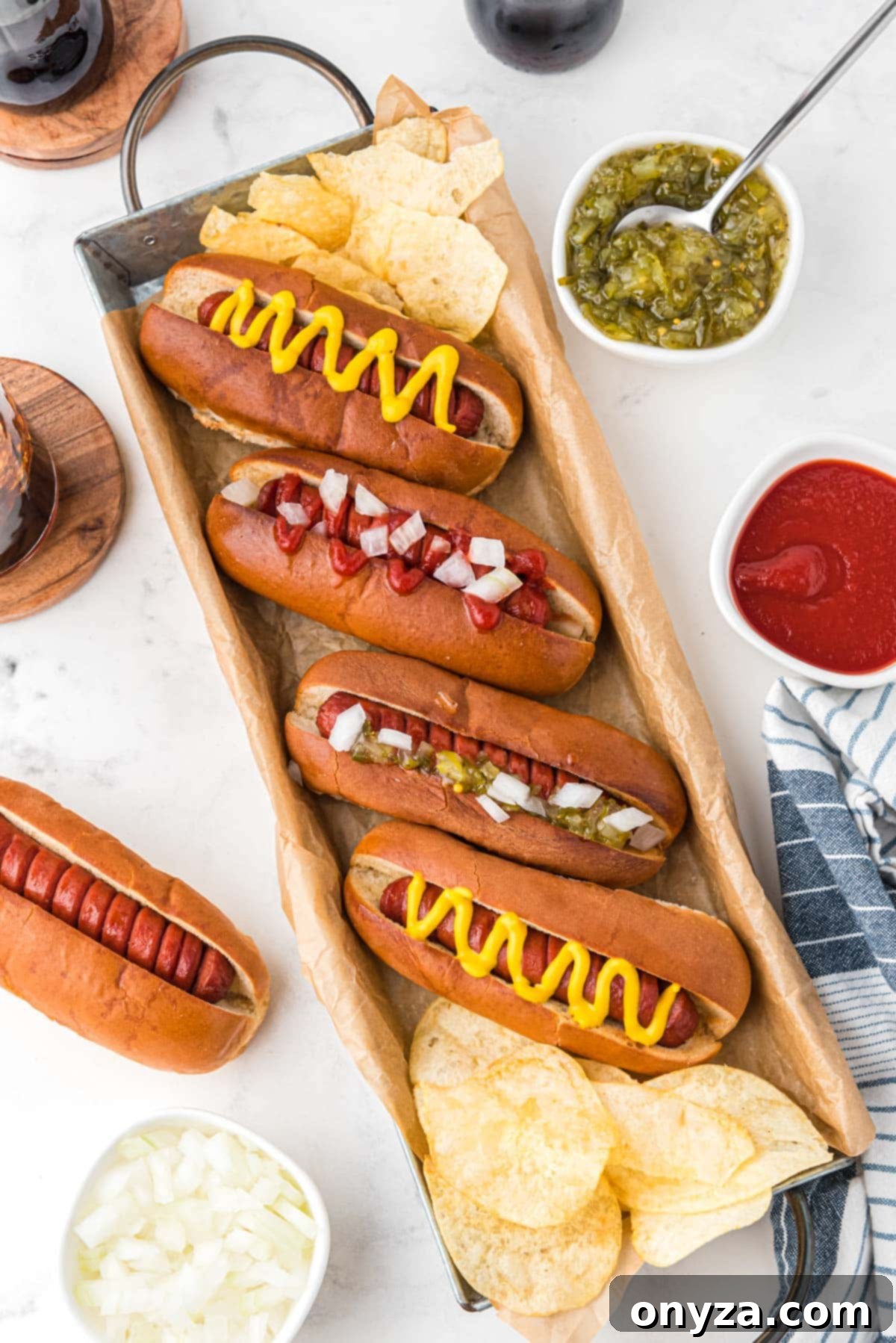 An inviting overhead photo of beautifully air fried hot dogs, served in toasted buns with a side of potato chips and various toppings, all neatly arranged in a parchment-lined serving tray.