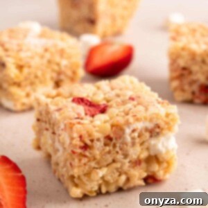 Sweet Strawberry Krispie Delights 13 Cut strawberry rice krispie treat squares on a beige background with strawberry wedges and miniature marshmallows