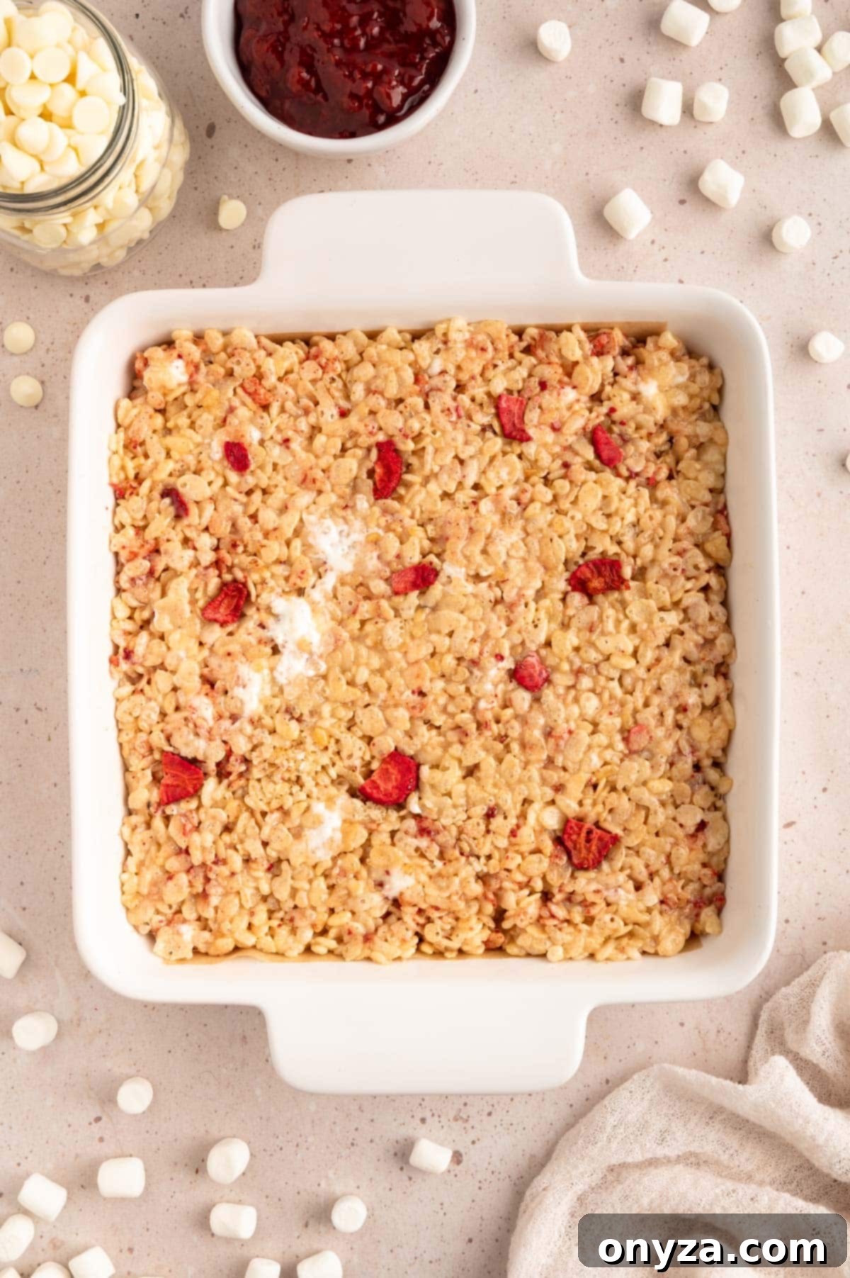 Sweet Strawberry Krispie Delights 7 Freshly pressed strawberry rice krispy treats nestled in a white square baking dish, awaiting setting