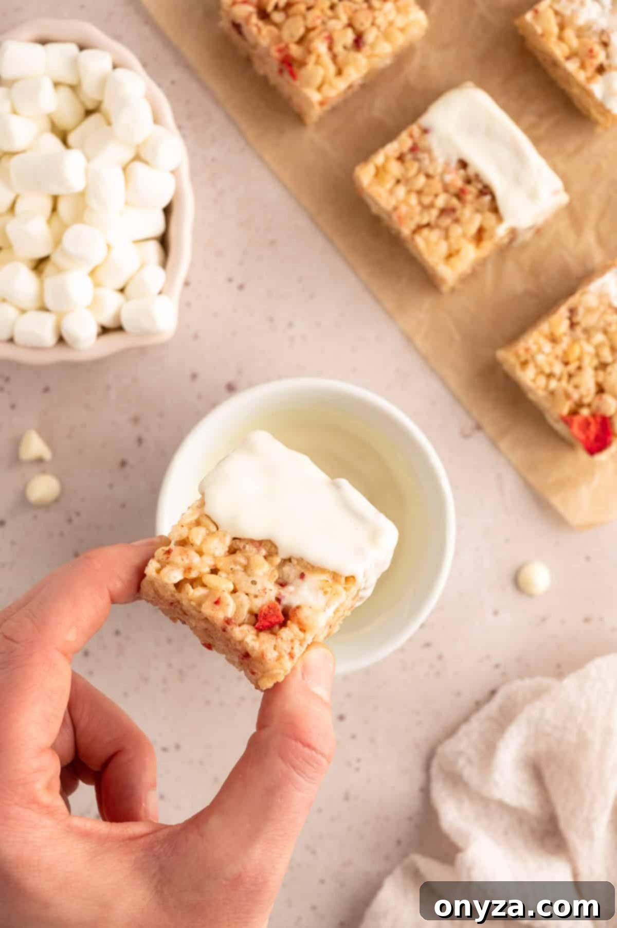 Sweet Strawberry Krispie Delights 10 Overhead perspective of a perfectly cut Strawberry Rice Krispie Treat being immersed into a bowl of smoothly melted white chocolate
