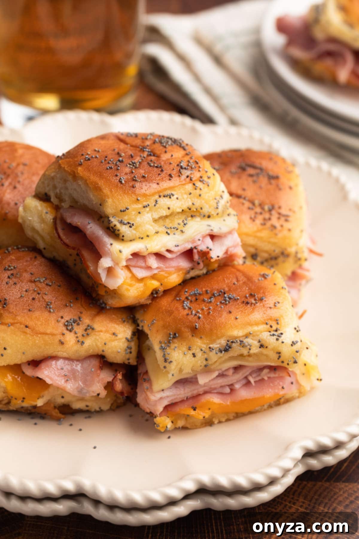baked ham and cheese sliders on a double stack of ivory ceramic plates, with a glass of beer in the background