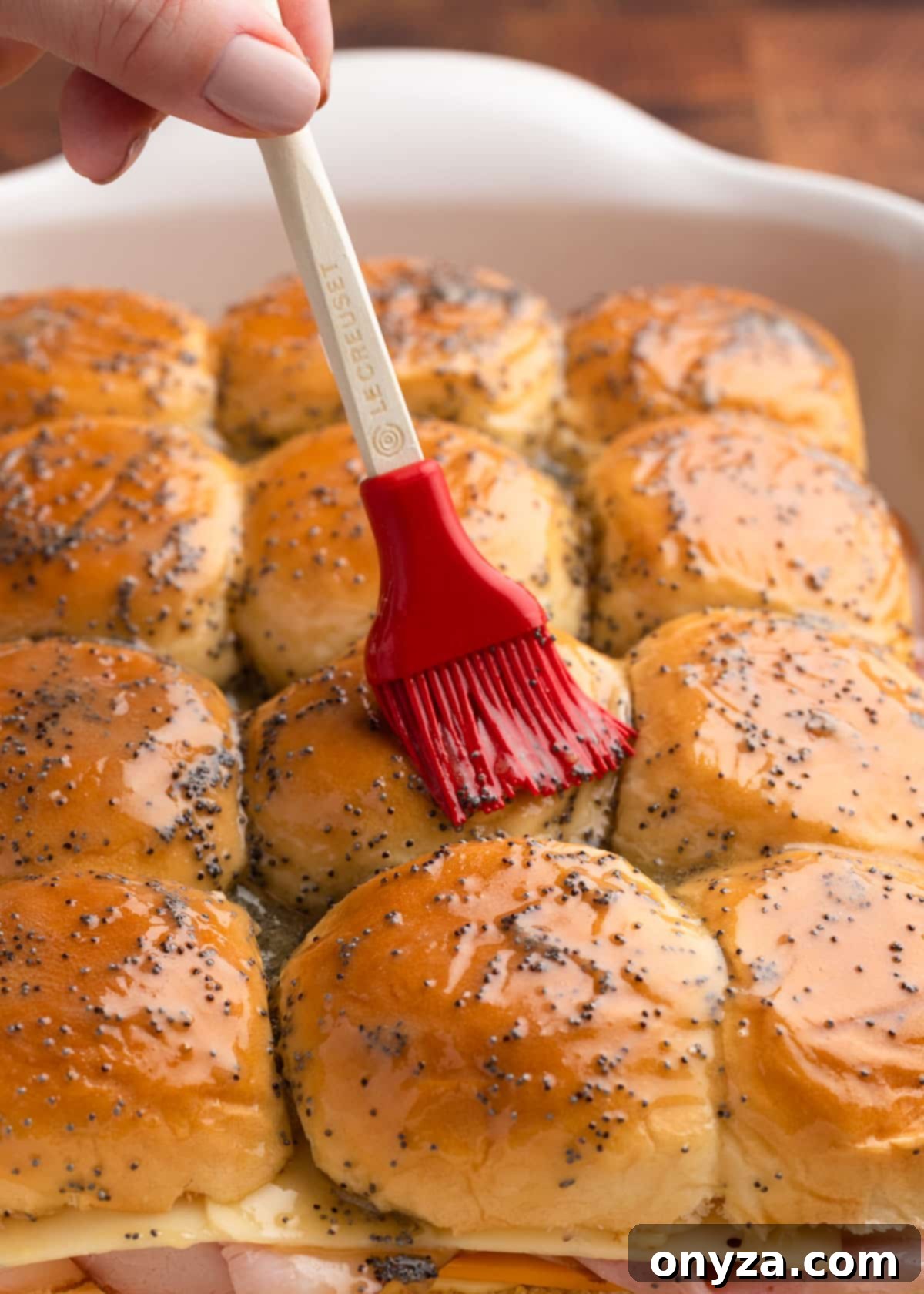 brushing poppy seed butter sauce onto unbaked sliders with a red silicone basting brush