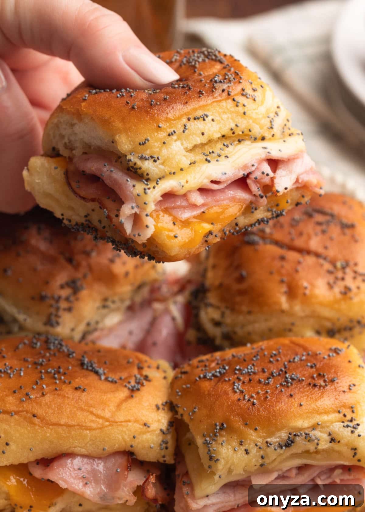 closeup of a baked ham and cheese slider being picked up from a platter