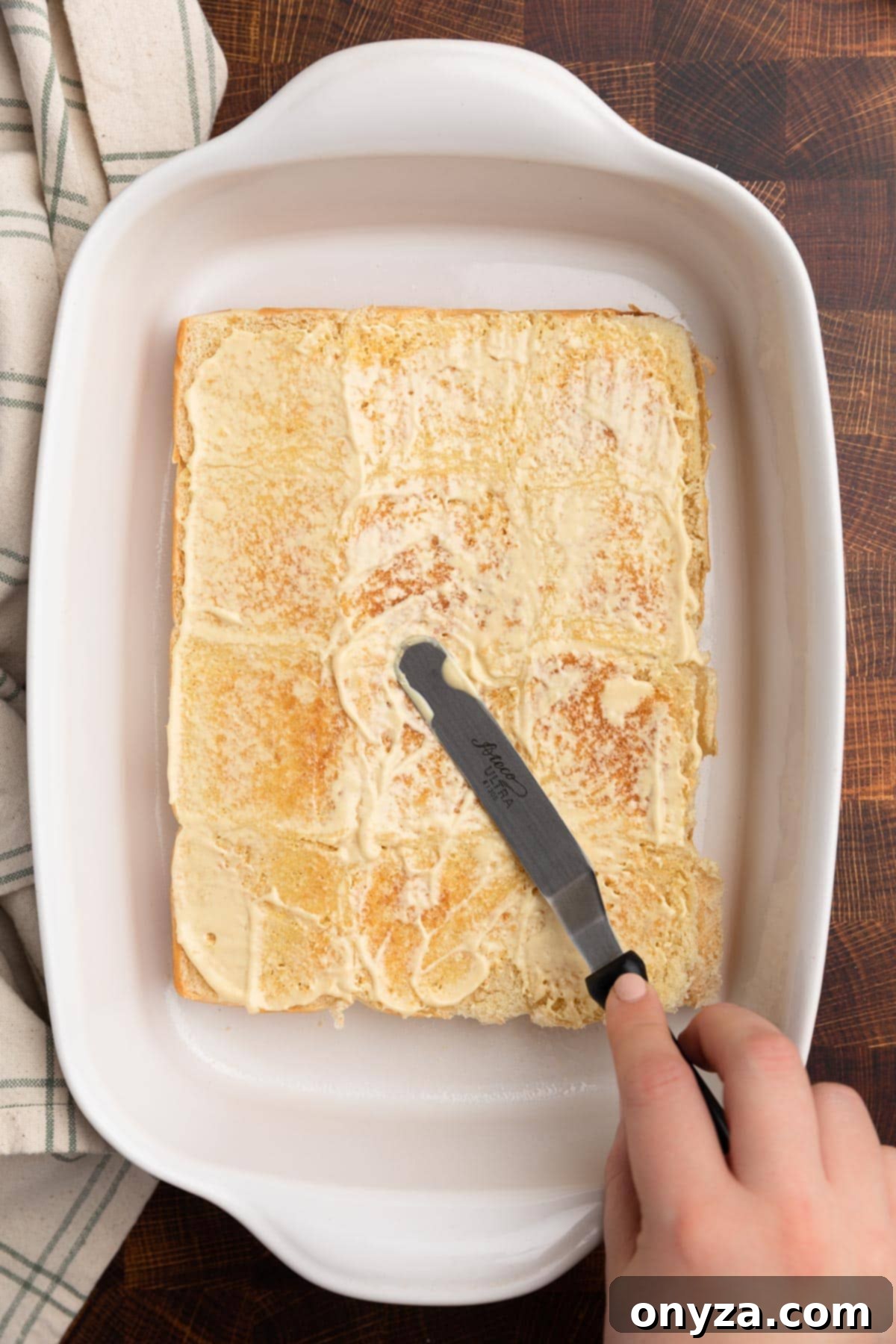 overhead photo of Dijon mayo being spread onto toasted slider rolls with a stainless steel icing spatula