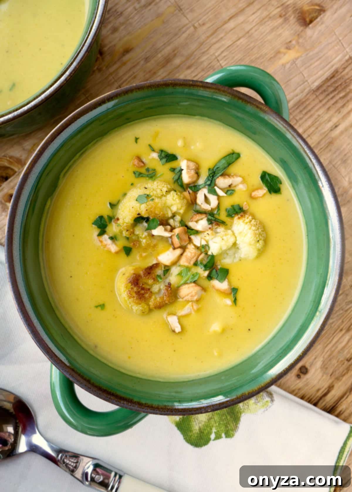 Aromatic Cauliflower Curry Puree 2 A vibrant bowl of creamy curried cauliflower soup, garnished with roasted cashews and fresh parsley, sitting on a rustic wooden board.