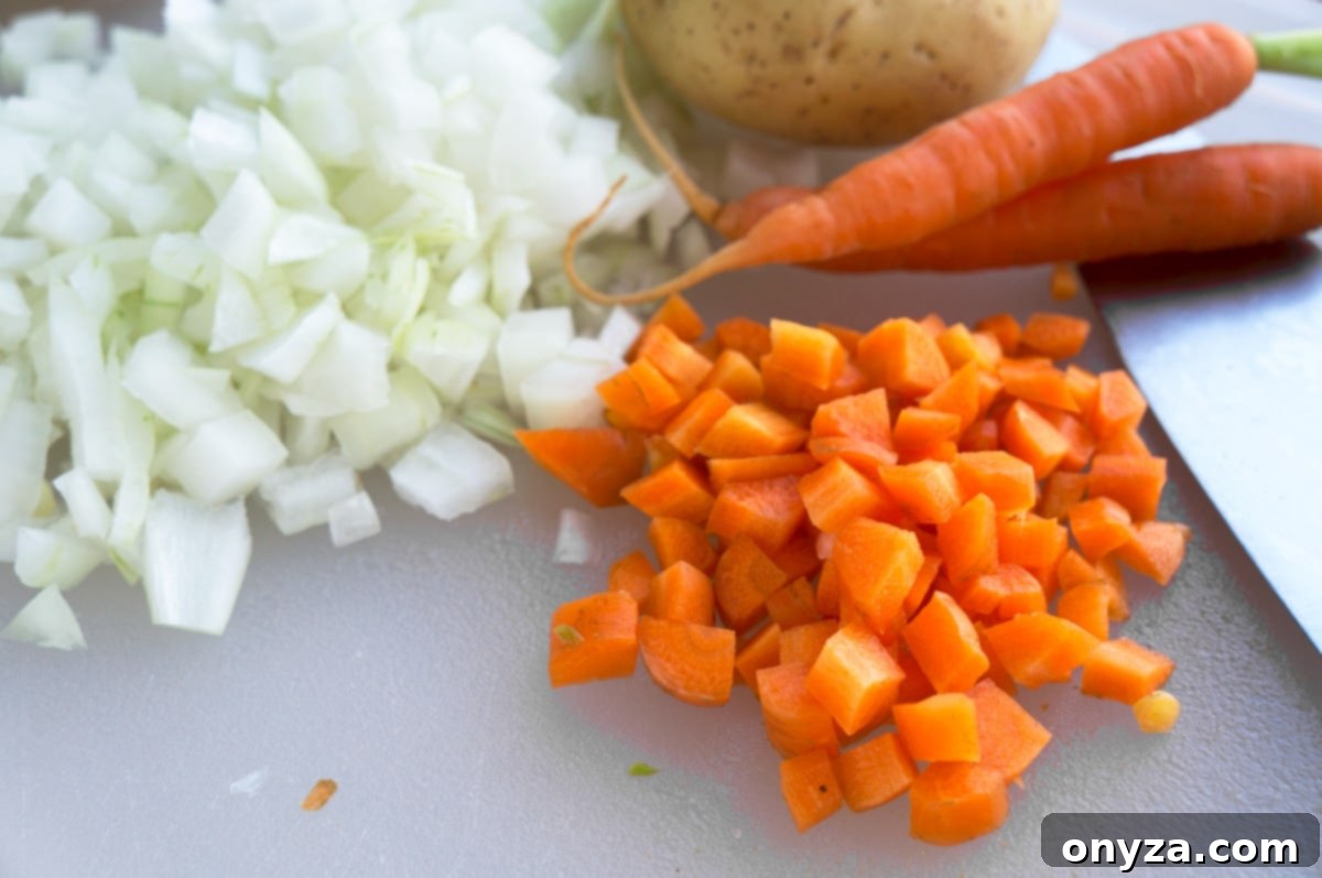 Aromatic Cauliflower Curry Puree 4 A selection of fresh soup ingredients including diced carrots, chopped yellow onion, and a peeled, diced Yukon Gold potato on a white cutting board.