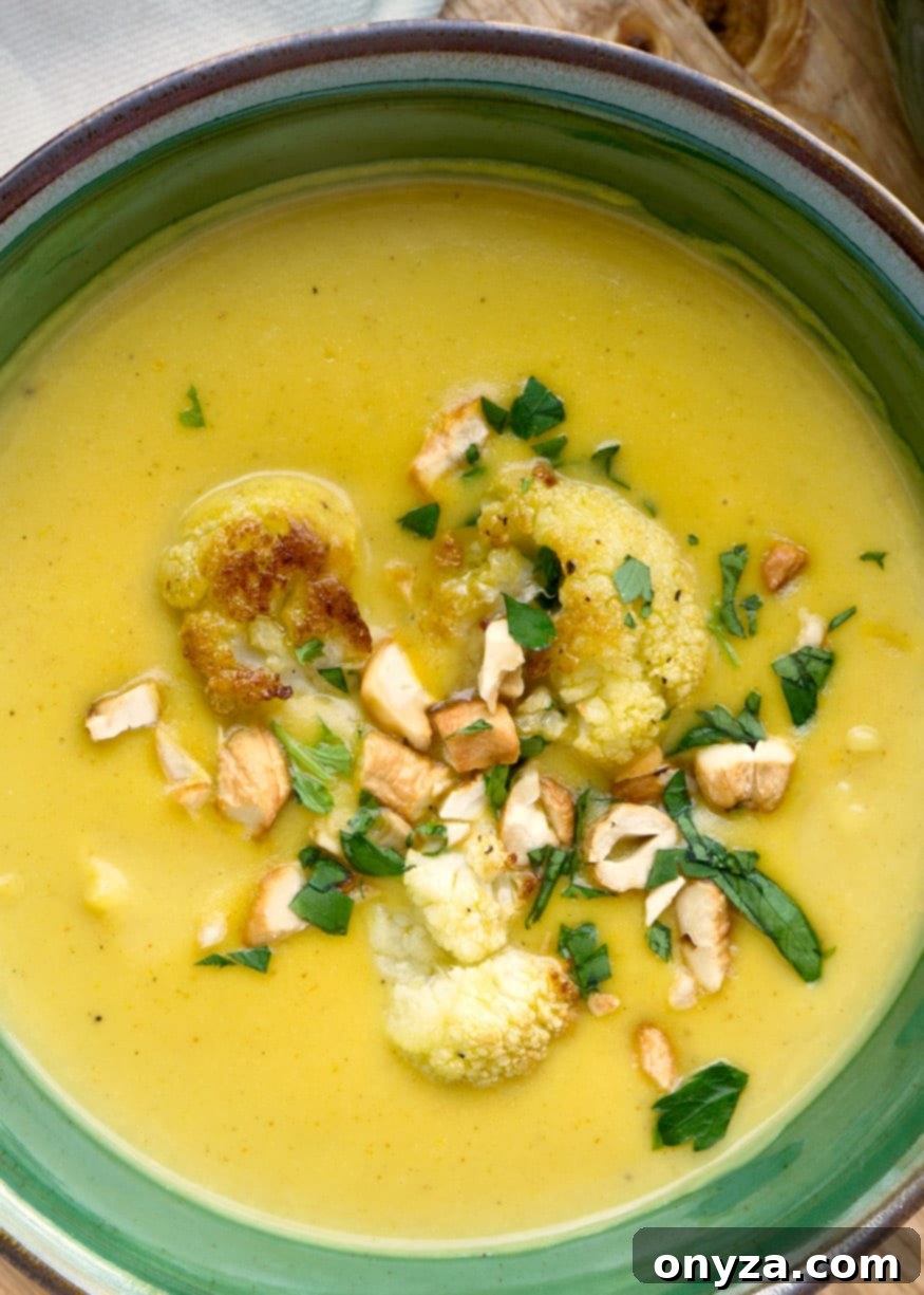Aromatic Cauliflower Curry Puree 7 A close-up of a steaming bowl of creamy curried cauliflower soup, garnished with crunchy roasted cashews and vibrant green parsley, in a green bowl.
