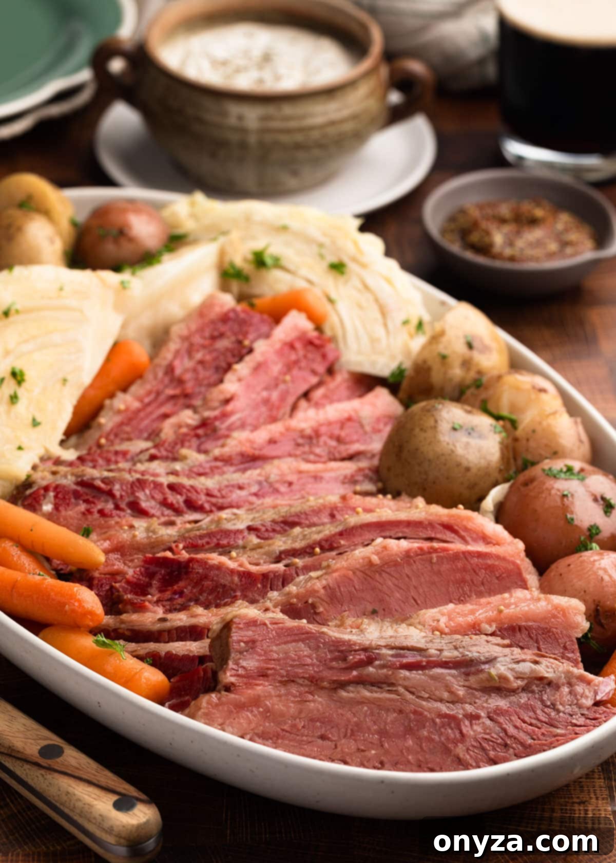 Effortless Slow Cooker Corned Beef and Cabbage 2 Sliced slow cooker corned beef on a white platter with baby potatoes, baby carrots, and cabbage wedges, ready to serve.