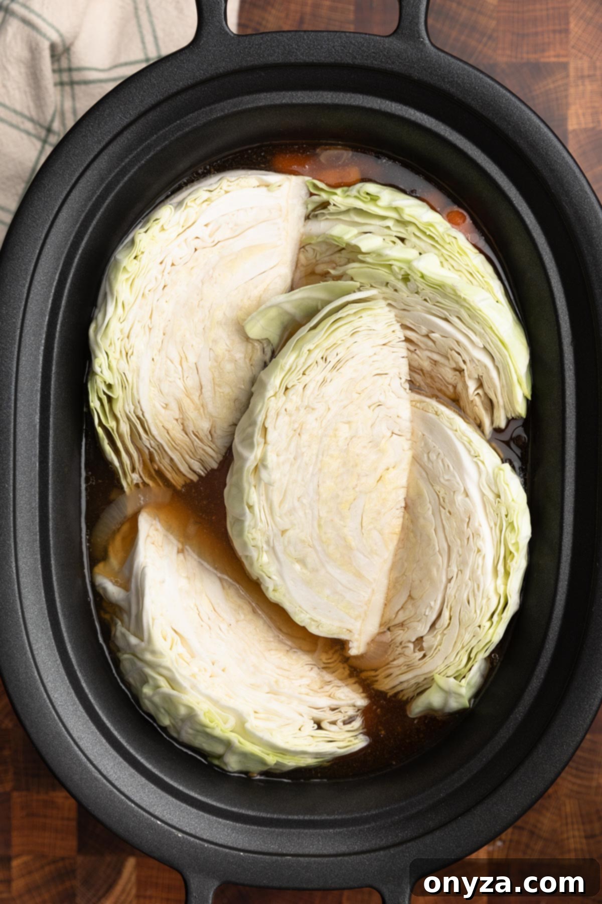 Effortless Slow Cooker Corned Beef and Cabbage 11 Overhead photo of uncooked cabbage wedges arranged over corned beef, potatoes, and carrots in a slow cooker insert.