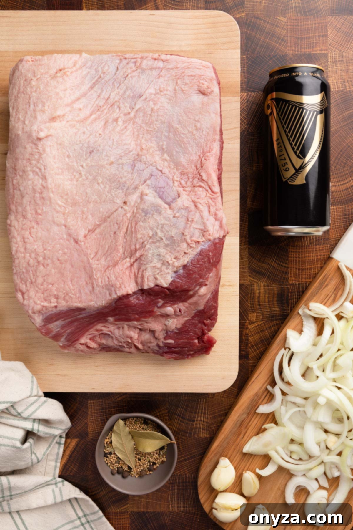 Effortless Slow Cooker Corned Beef and Cabbage 3 Overhead shot of an uncooked corned beef brisket, a can of Guinness Draught, sliced onions, and a bowl of pickling spices, ready for slow cooking.