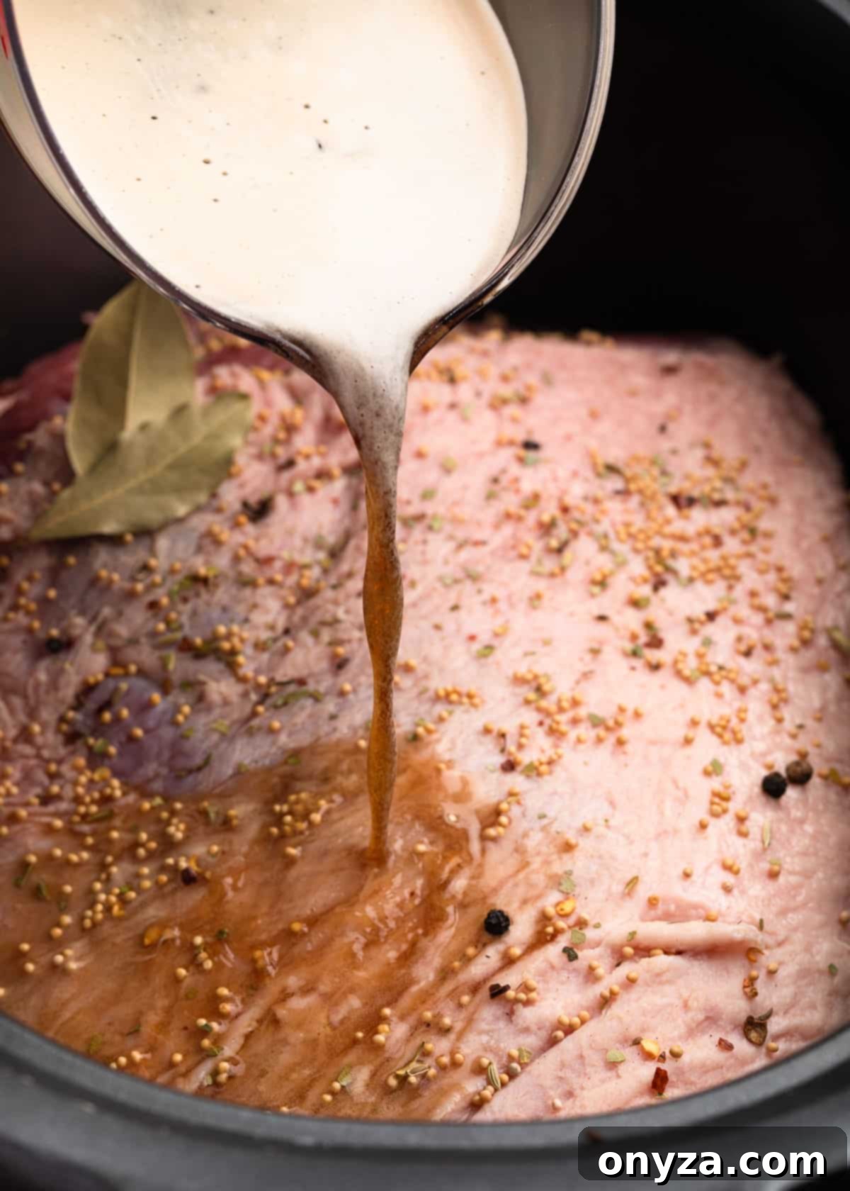 Effortless Slow Cooker Corned Beef and Cabbage 6 Stout beer being poured from a liquid measuring cup over an uncooked corned beef brisket in a slow cooker insert.