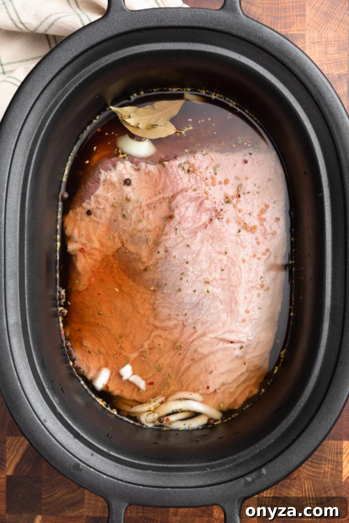 Effortless Slow Cooker Corned Beef and Cabbage 8 Overhead photo of an uncooked corned beef brisket fully submerged in liquid within a slow cooker insert.