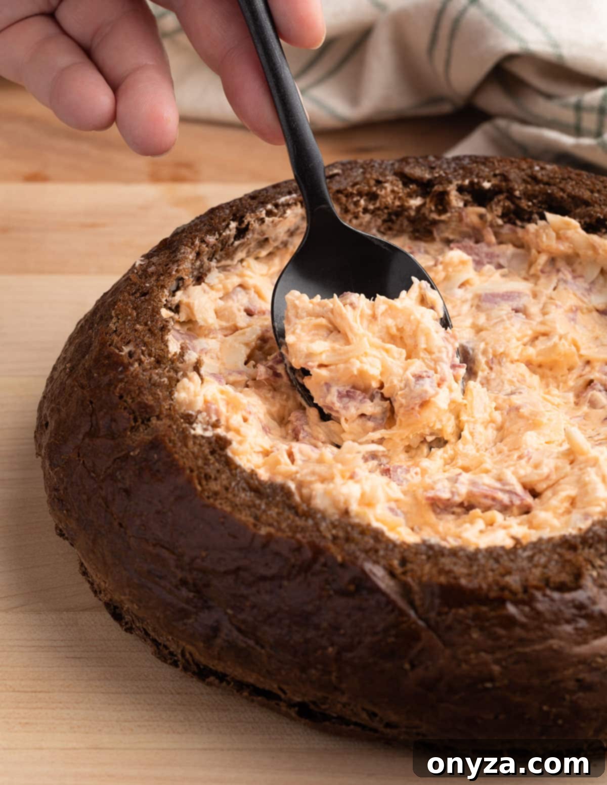 Irresistible Reuben Dip 6 reuben dip being spooned into a pumpernickel bread bowl with a black spoon
