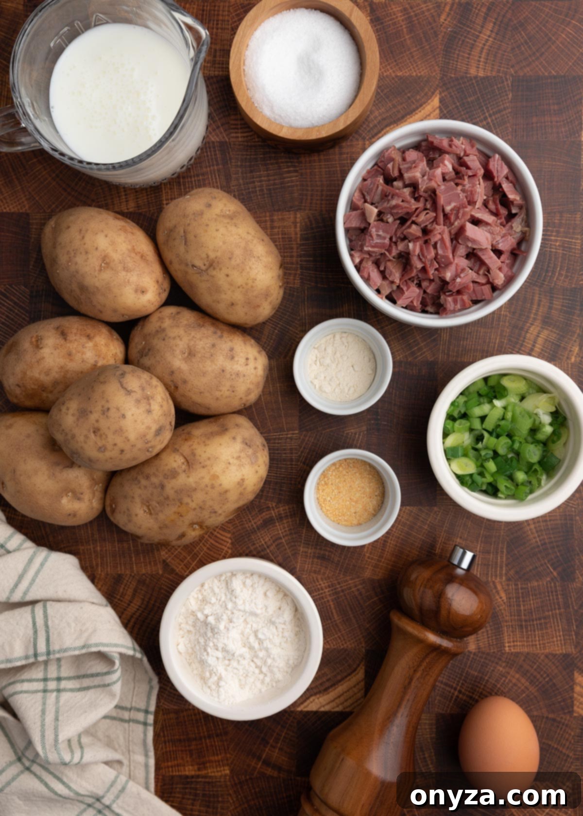 Golden Corned Beef Potato Fritters 3 An overhead shot showcasing key ingredients for making corned beef potato cakes: russet potatoes, a bowl of shredded corned beef, a bowl of thinly sliced scallions, and small bowls of various spices, all arranged on a rustic wooden butcher block surface.