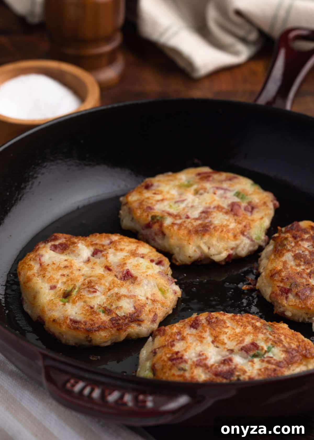 Golden Corned Beef Potato Fritters 8 Freshly fried corned beef and potato cakes, perfectly golden-brown and crispy, arranged neatly in a black enameled cast iron skillet.
