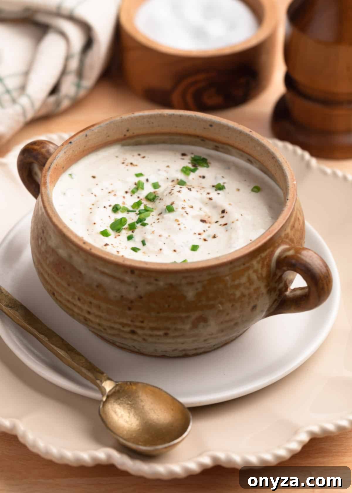 creamy horseradish sauce in a tan ceramic crock on a small white plate with a brass spoon