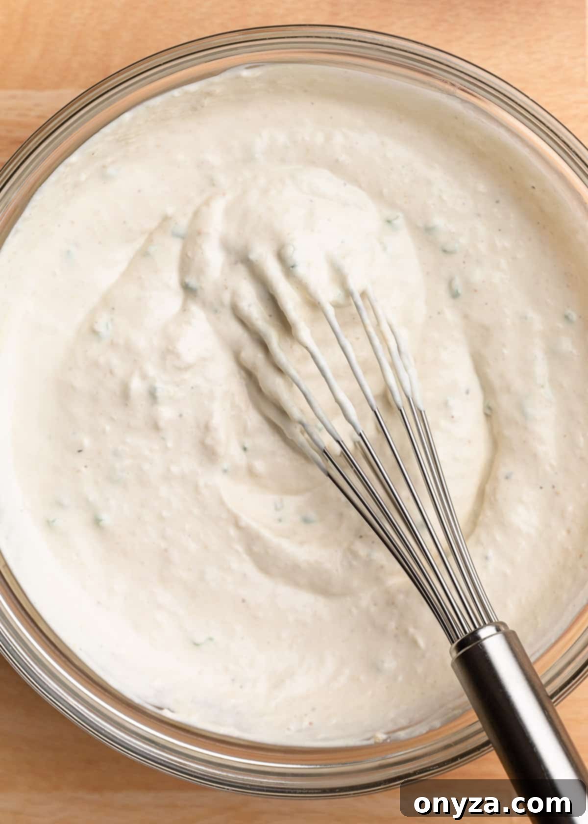 closeup overhead photo of horseradish cream sauce being mixed in a glass bowl with a stainless steel whisk