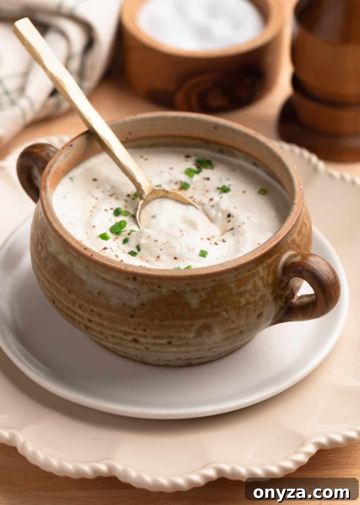 creamy horseradish sauce in a tan crock on a white plate with a brass spoon dipped into the sauce