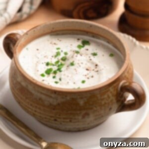 creamy horseradish sauce with chives in a tan ceramic crock