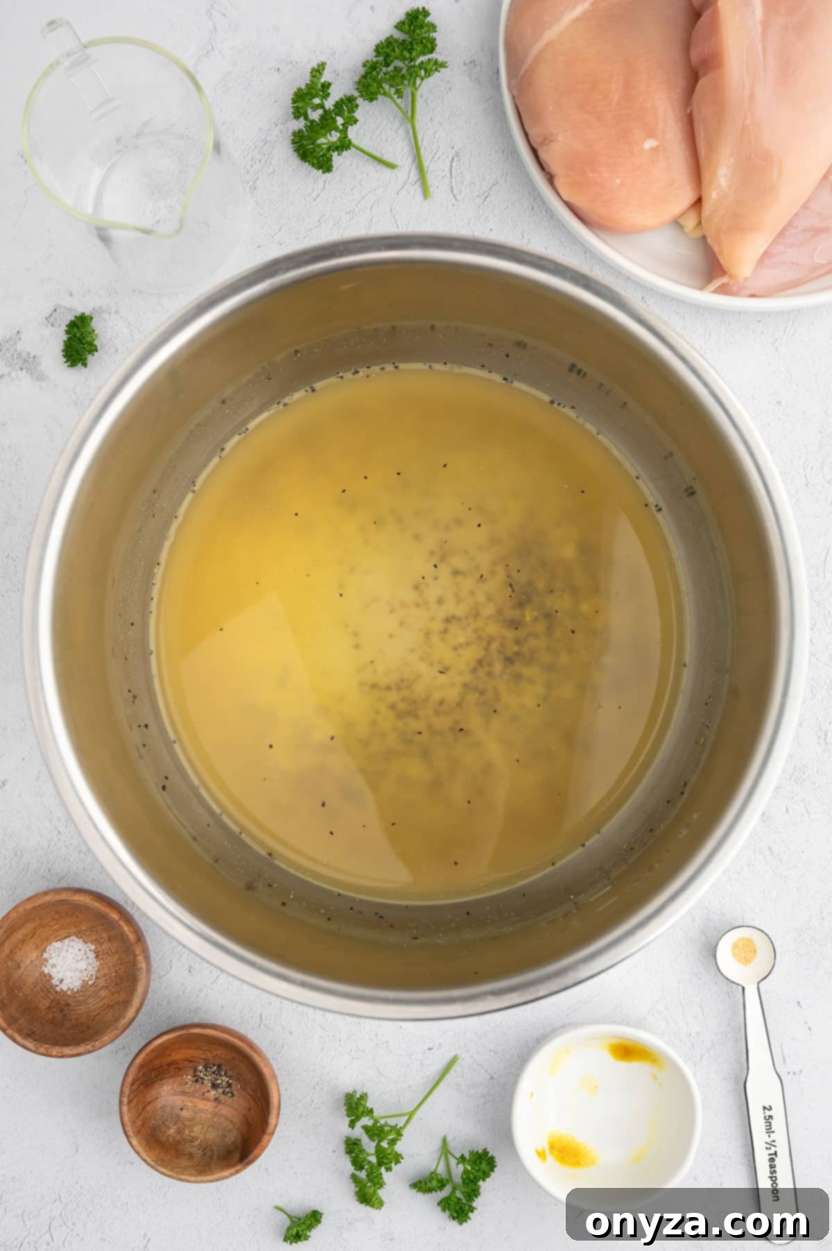 overhead photo chicken bouillon in an instant pot insert surrounded by used bowls of seasonings and a plate of chicken breasts