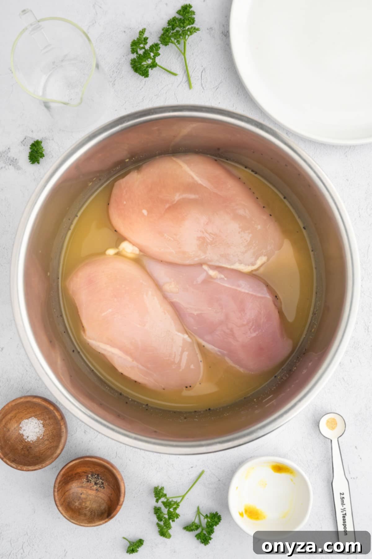 overhead photo of raw chicken breasts sitting in seasoned chicken bouillon in a stainless steel Instant Pot insert
